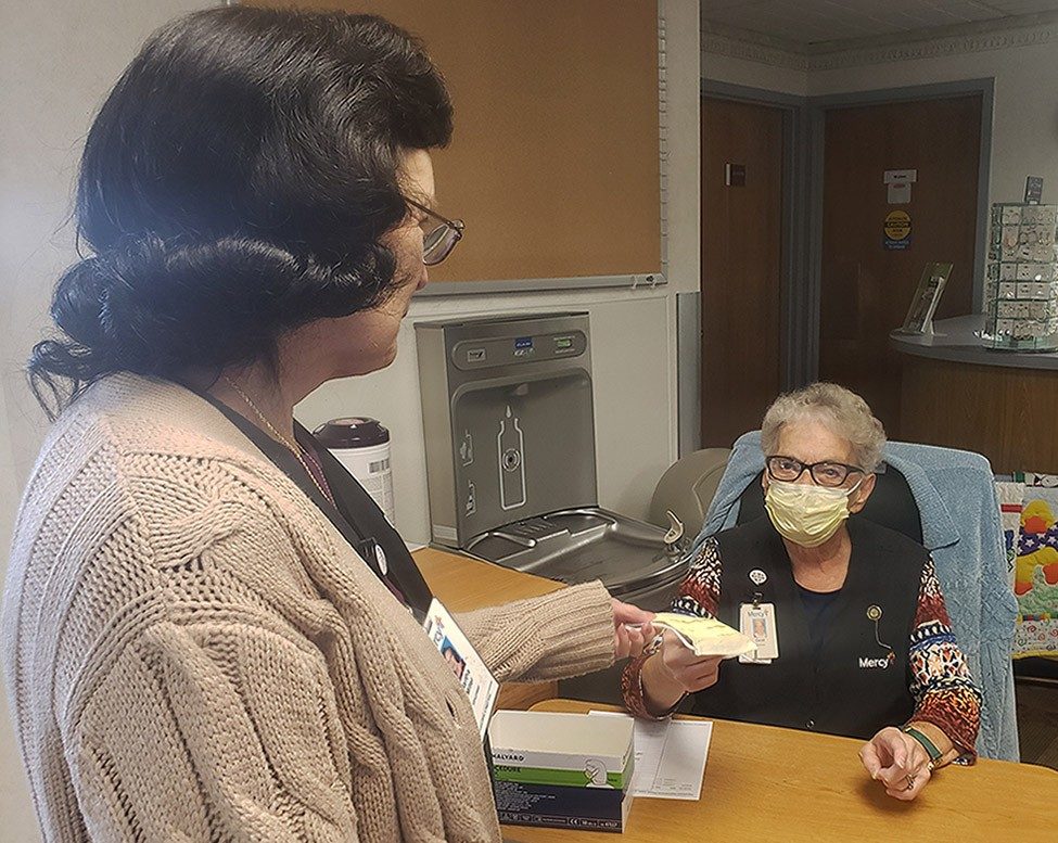 Volunteer Marti Miller grabs a mask from fellow auxilian Carol Iseminger as she gets ready for her shift at Mercy St. Francis Hospital.